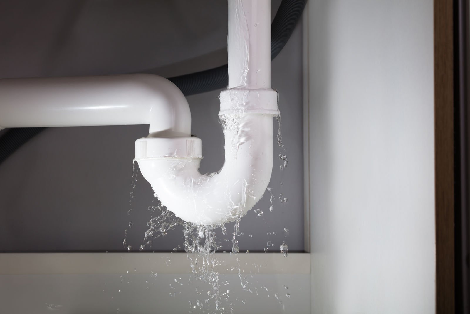Burst pipe spraying water under a kitchen sink during an emergency repair