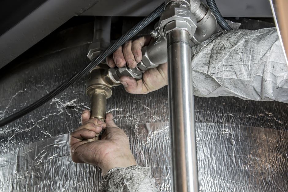 Plumber tightening copper fittings with a wrench under a bathroom basin